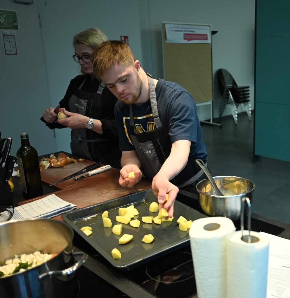 Ein junger Mann verteilt geschnittene Kartoffeln auf einem gefetteten Backblech