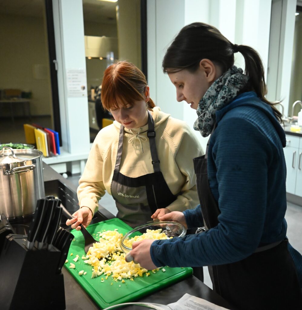 Zwei junge Frauen füllen die geschnittenen Zutaten in eine Glasschüssel