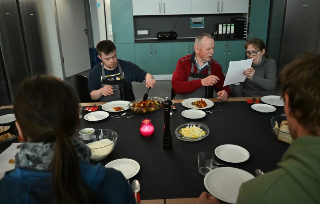 Die Teilnehmer sitzen beim Essen am Tisch und zwei Personen besprechen ein Rezept